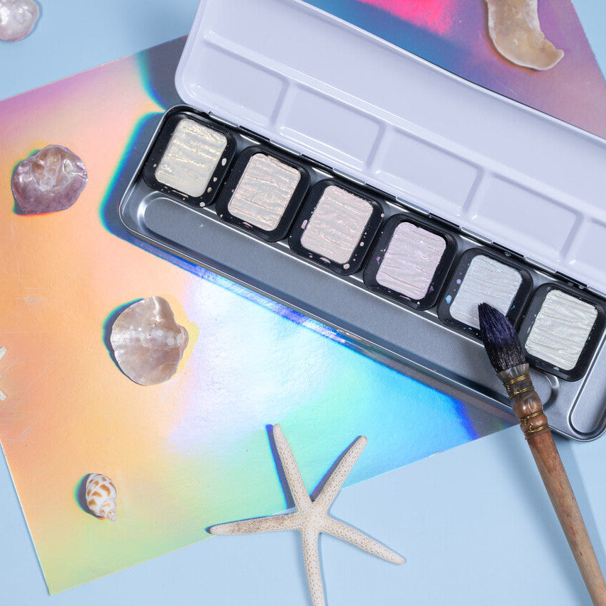 Set of watercolor pans with a brush on a colorful card with starfish designs.